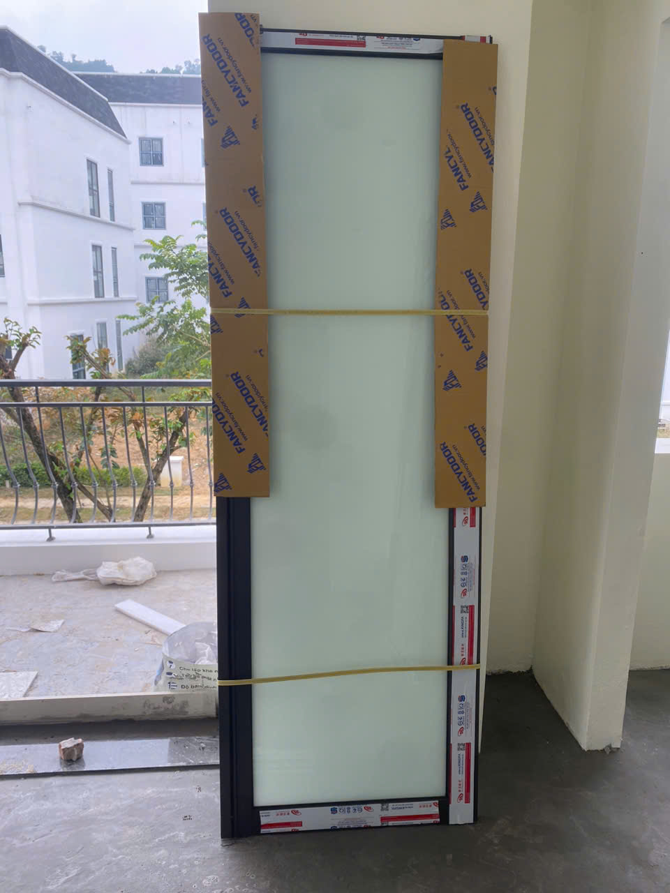 Cửa kính khung nhôm Fancydoor mới, còn bọc bảo vệ, đặt trong nhà gần ban công